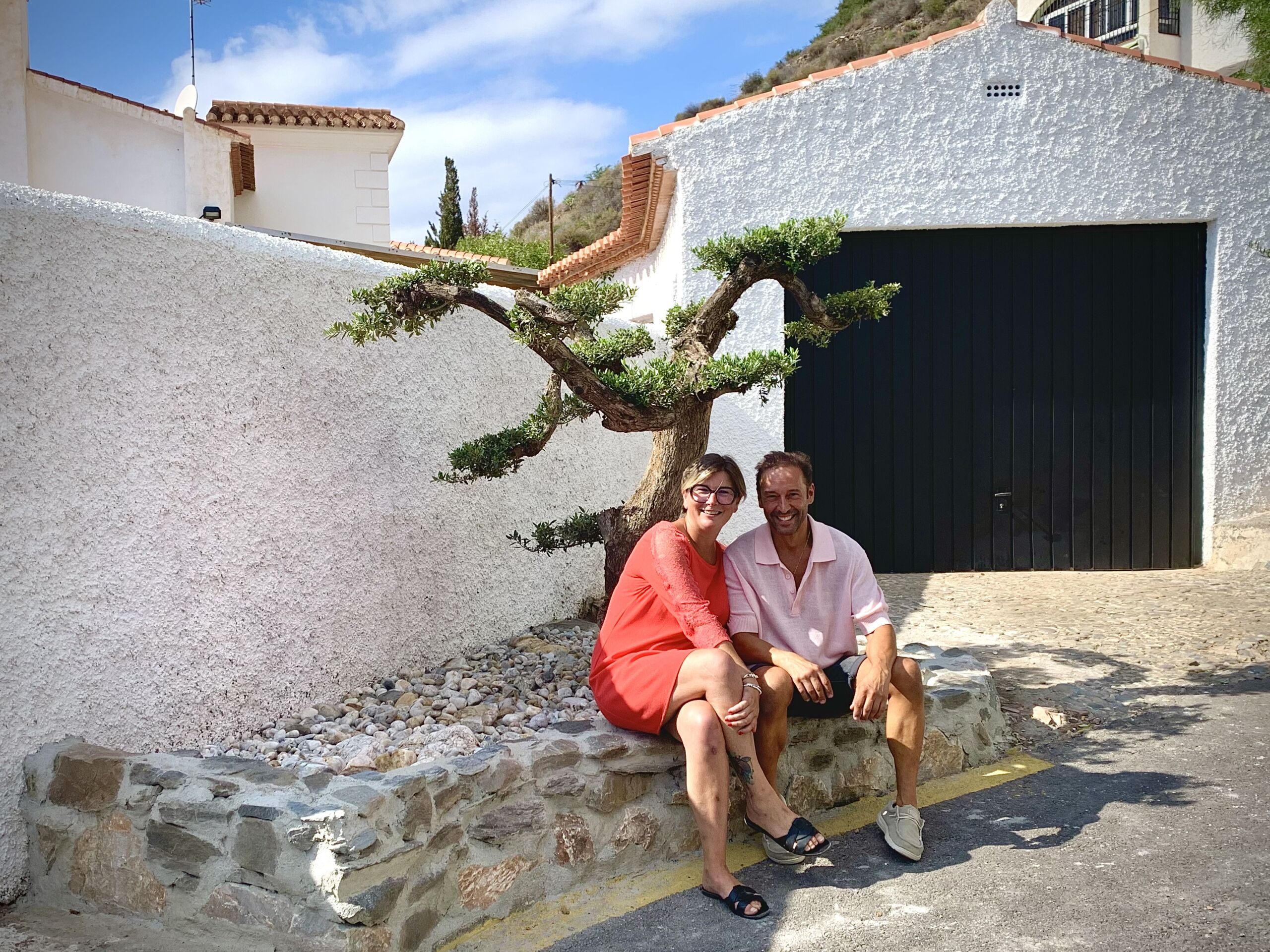 Olivier Flores Sánchez and Laetitia Tordeurs sitting beside the ornamental olive tree they planted outside Casa Nº 41 in Urbanización Alfa-Mar