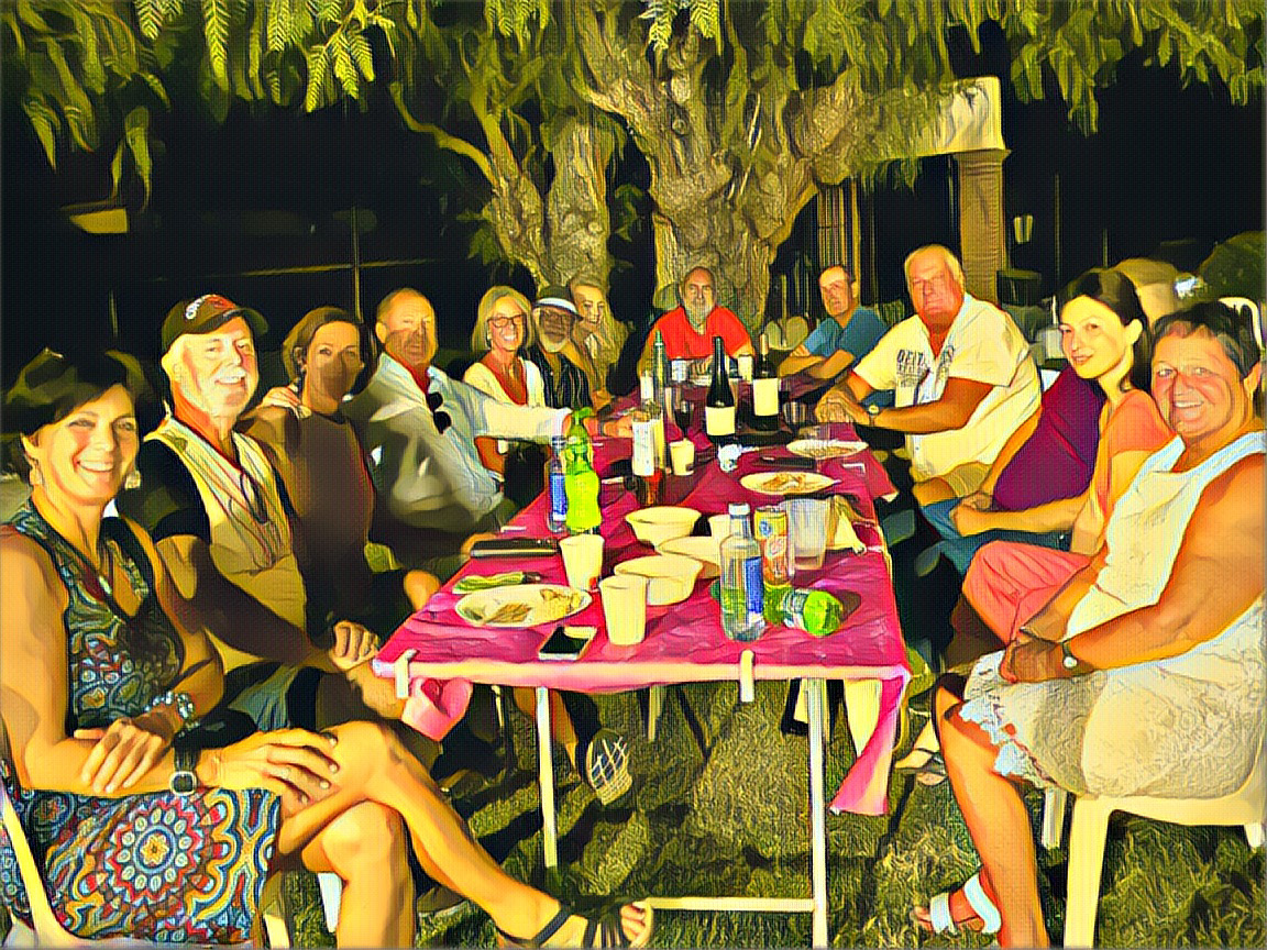 Neighbors and friends gathered around a colorful table under the trees